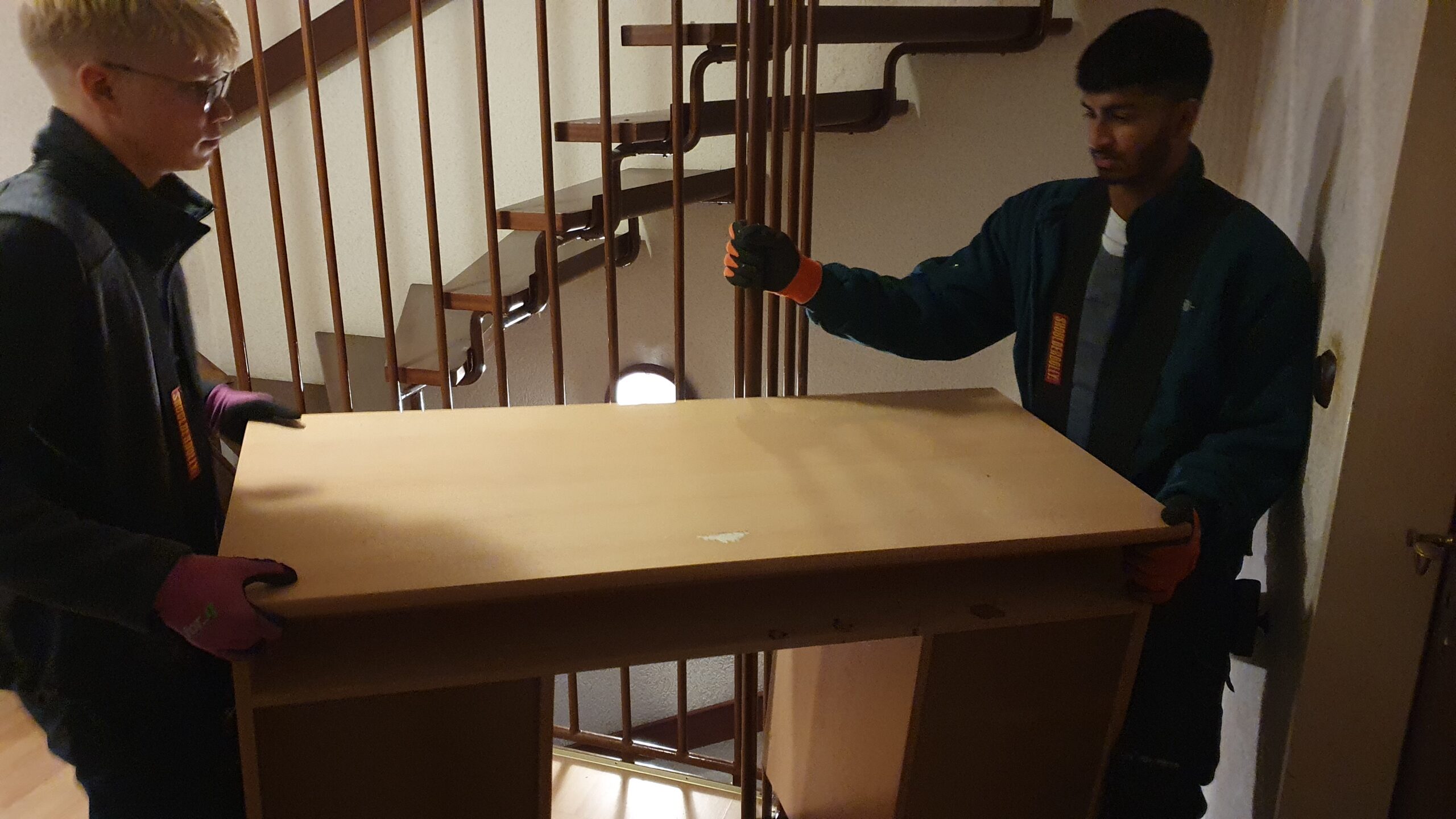 Zwei Mitarbeiter transportieren einen Schreibtisch durch ein Treppenhaus