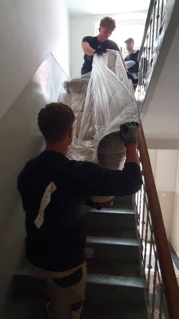 Mitareiter von Martens Umzüge tragen eine folierte Couch ein Treppenhaus hinunter