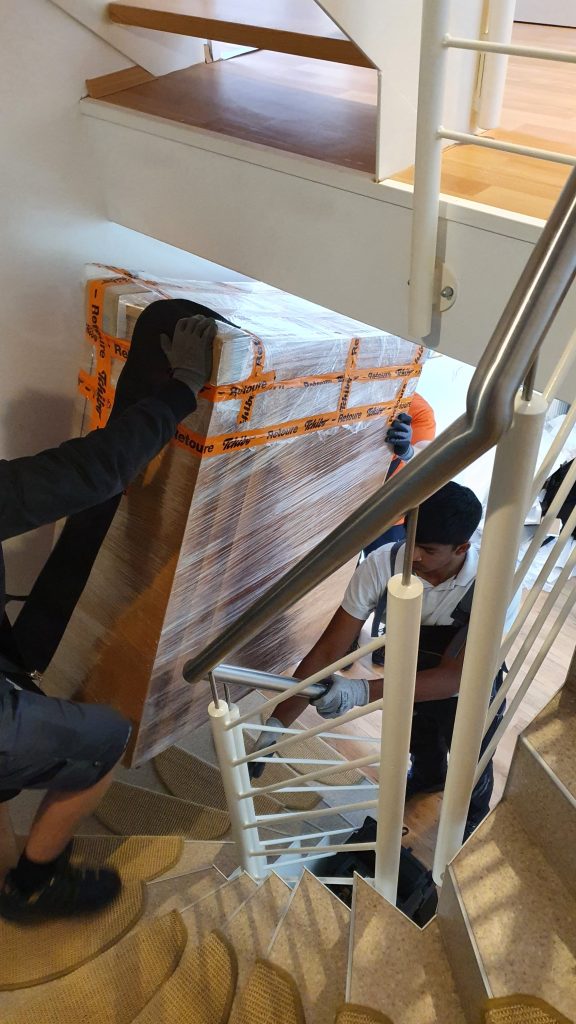 Mitarbeiter von Martens Umzüge tragen eingroßes Möbelstück über eine enge Treppe