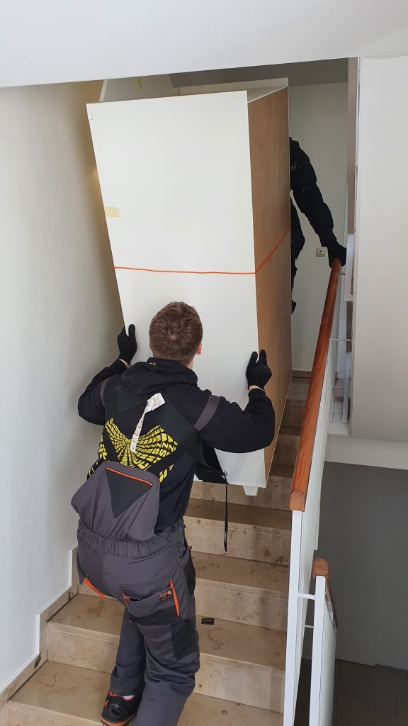 Mitarbeiter von Martens Umzüge tragen einen Schrank durch ein Treppenhaus