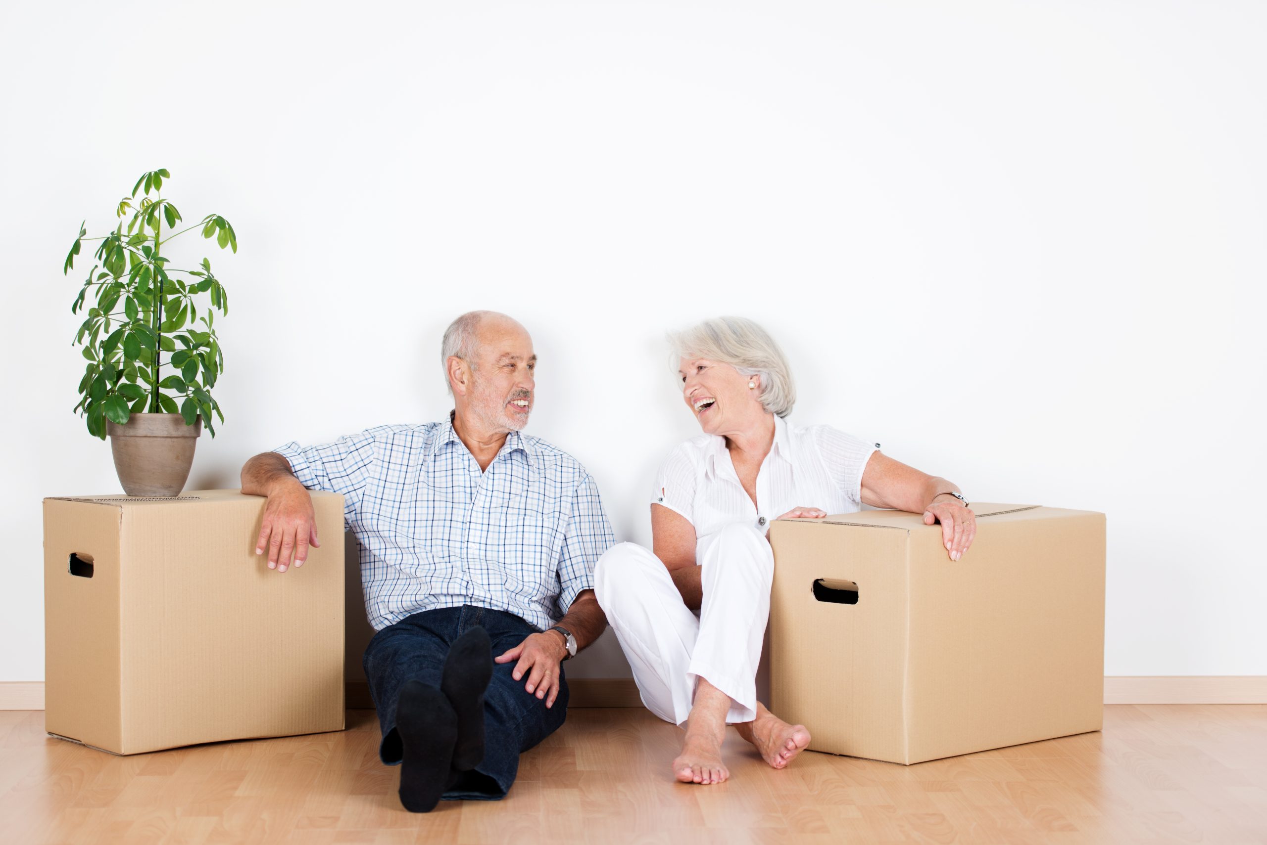 Senioren sitzen neben Umzugskartons in einer Wohnung